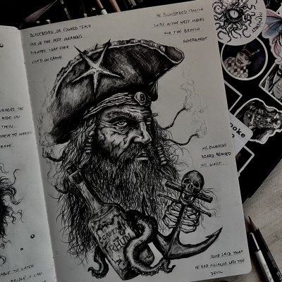 Pirate drawing in a sketchbook with a dark big hat, a starfish and a bottle of rum